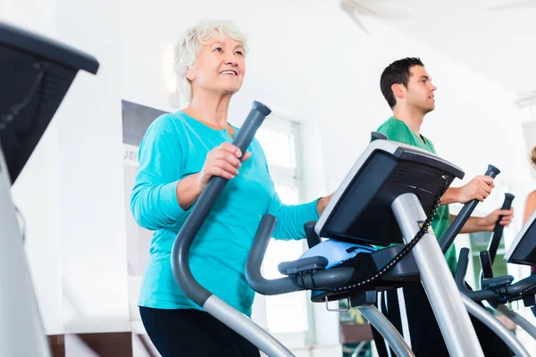 Mujer mayor en entrenamiento elíptico haciendo ejercicio en el gimnasio —  Fotos de Stock