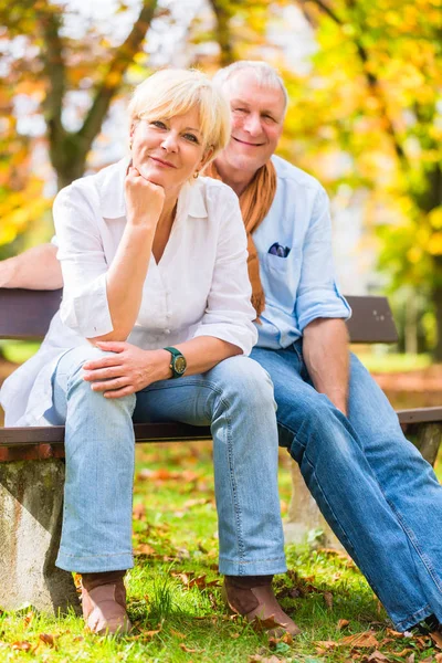 Senior paar zittend op deel bankje in herfst — Stockfoto