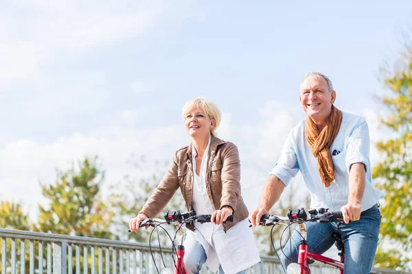 Senior couple with bicycles on bridge — Stock Photo, Image