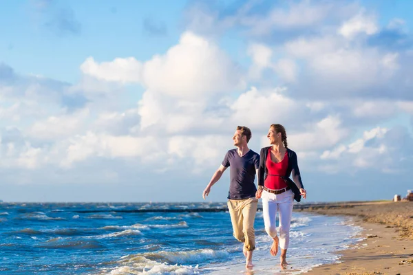 Coppia che corre tra sabbia e onde in spiaggia — Foto Stock