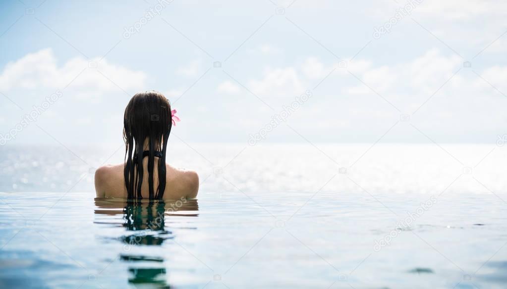 Woman tourist in infinity pool of hotel resort at ocean
