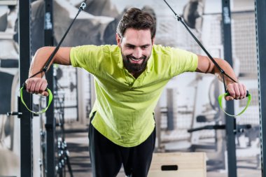 Fonksiyonel eğitim spor salonu içinde yüzük pushup yapan erkek