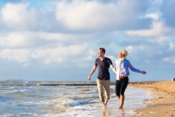 Pareja corriendo a través de arena y olas en la playa — Foto de Stock