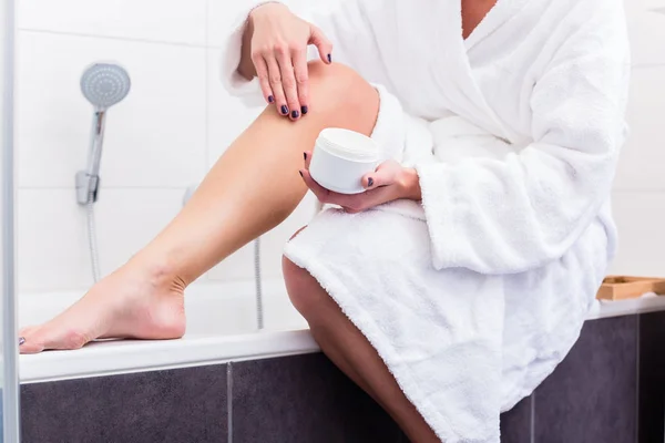 Donna seduta all'orlo di vasca da bagno che si mette la lozione su gambe — Foto Stock