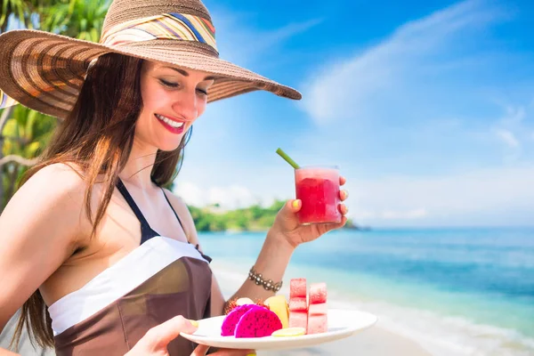 Mujer en la playa tropical comiendo fruta para el desayuno —  Fotos de Stock