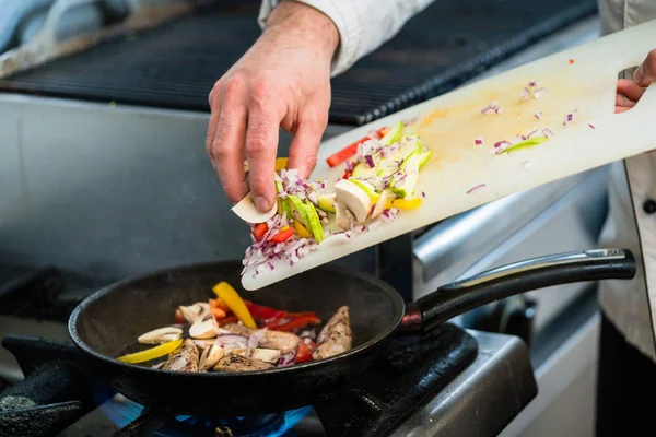 Chef putting ingredients to pan in restaurant kitchen — Stock Photo, Image