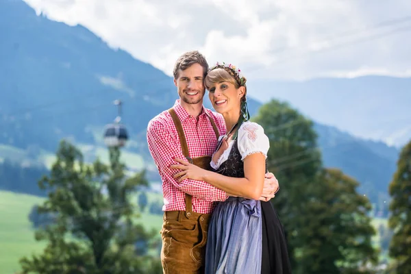 Casal em Tracht de pé no prado em alp montanhas — Fotografia de Stock