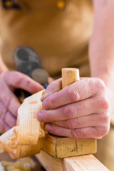 Carpinteiro com plaina de madeira e peça de trabalho em carpintaria — Fotografia de Stock