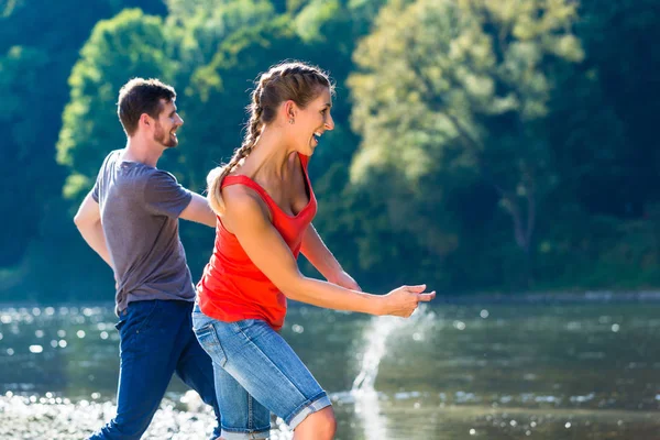 Man and woman skimming stones on river — Stock Photo, Image