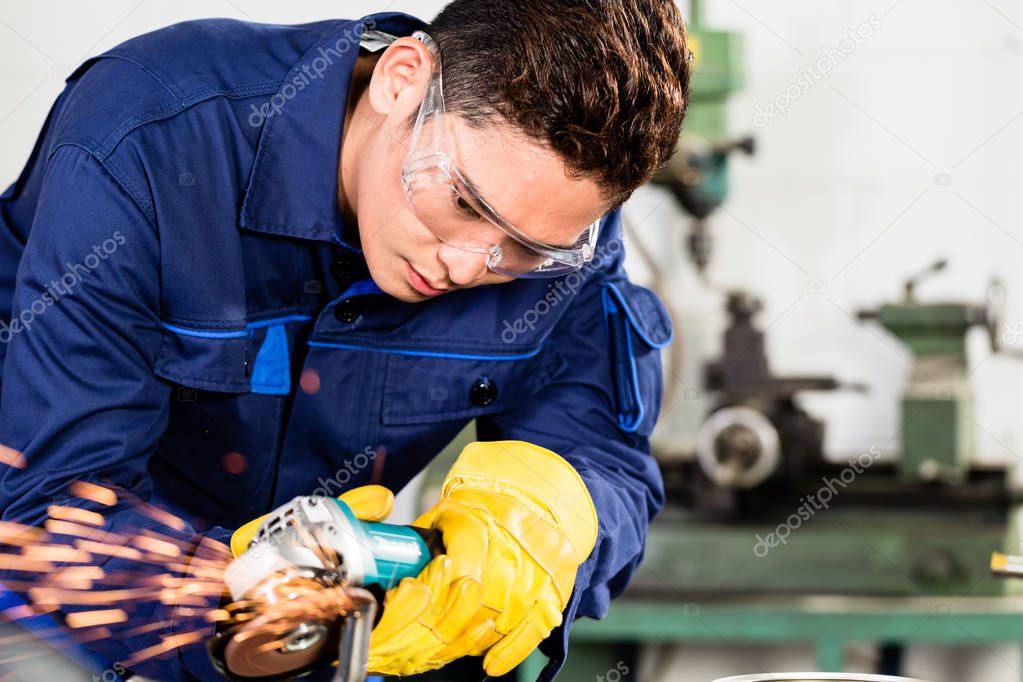 Asian worker grinding metal in manufacturing plant