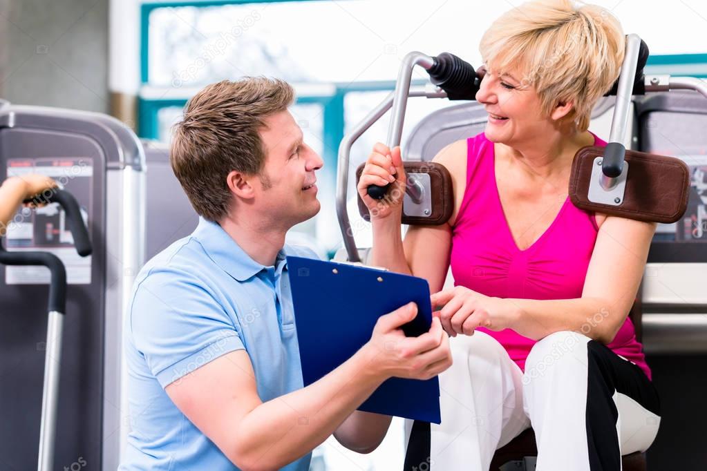Trainer in gym assisting senior woman exercising