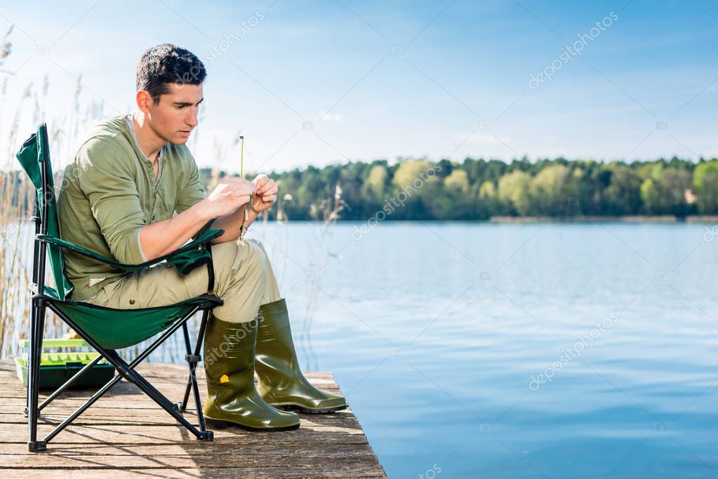 Man fishing at lake fixing lure at angling rod