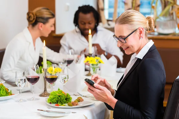 Frau beim Geschäftsessen checkt Mails am Telefon — Stockfoto