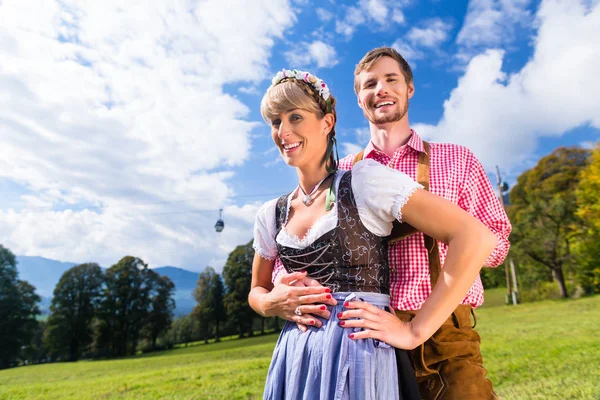 Casal em Tracht de pé no prado em alp montanhas — Fotografia de Stock