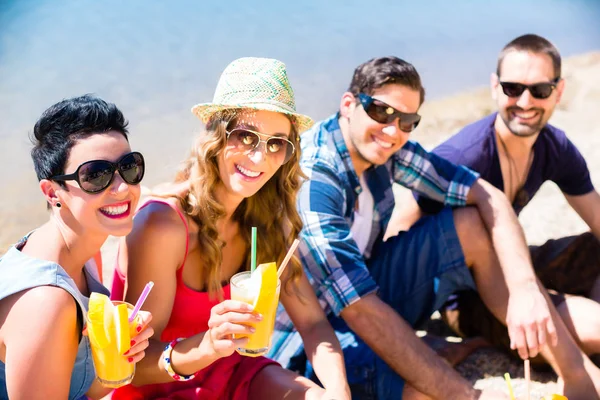 Vier Freunde sitzen mit Cocktails am Seestrand — Stockfoto