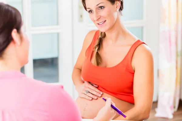 Aanstaande moeder met haar hand op zwangere buik raadpleging midw — Stockfoto