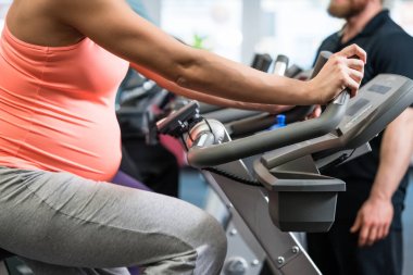 Spor salonunda bisiklet süren hamile bir kadın. 
