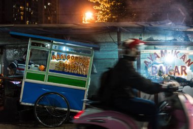 Bir adam sokakta geleneksel gıda ile bir scooter sürme yan görünüm Jakarta geceleri duraksıyor.