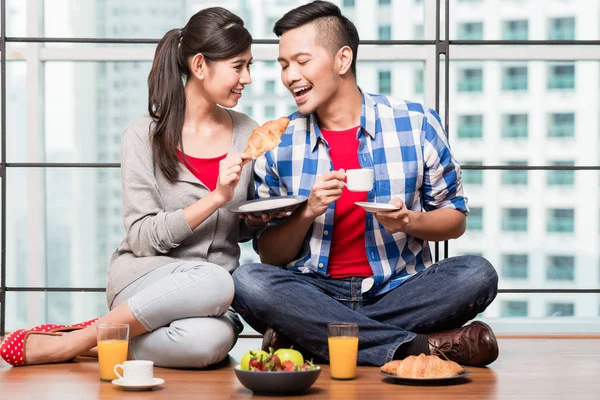 Junges Indonesisches Paar Sitzt Auf Dem Boden Und Isst Croissants — Stockfoto