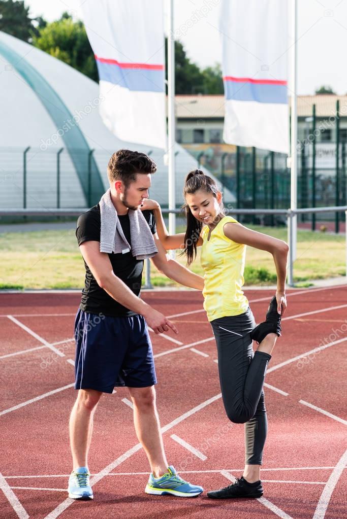 Man and woman on track of sports arena doing stretching exercises