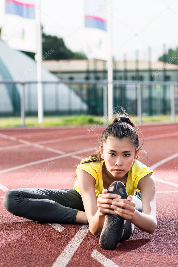 woman athlete stretching on racing track before running 
