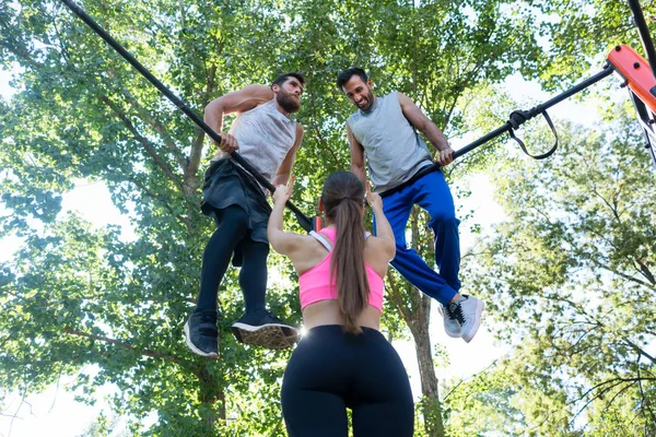 一个适合女性的低角度后视图在一个现代健美操公园的极端锻炼中 她的两个男性朋友在户外的表现大拇指 — 图库照片
