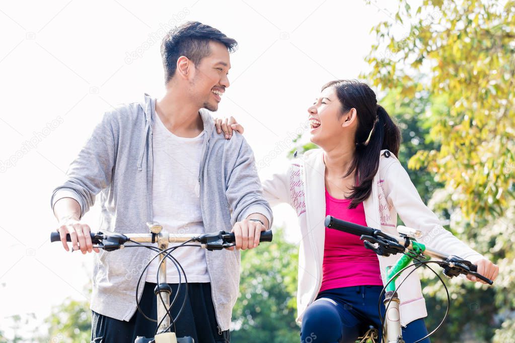 Young Asian couple laughing together while riding bicycles