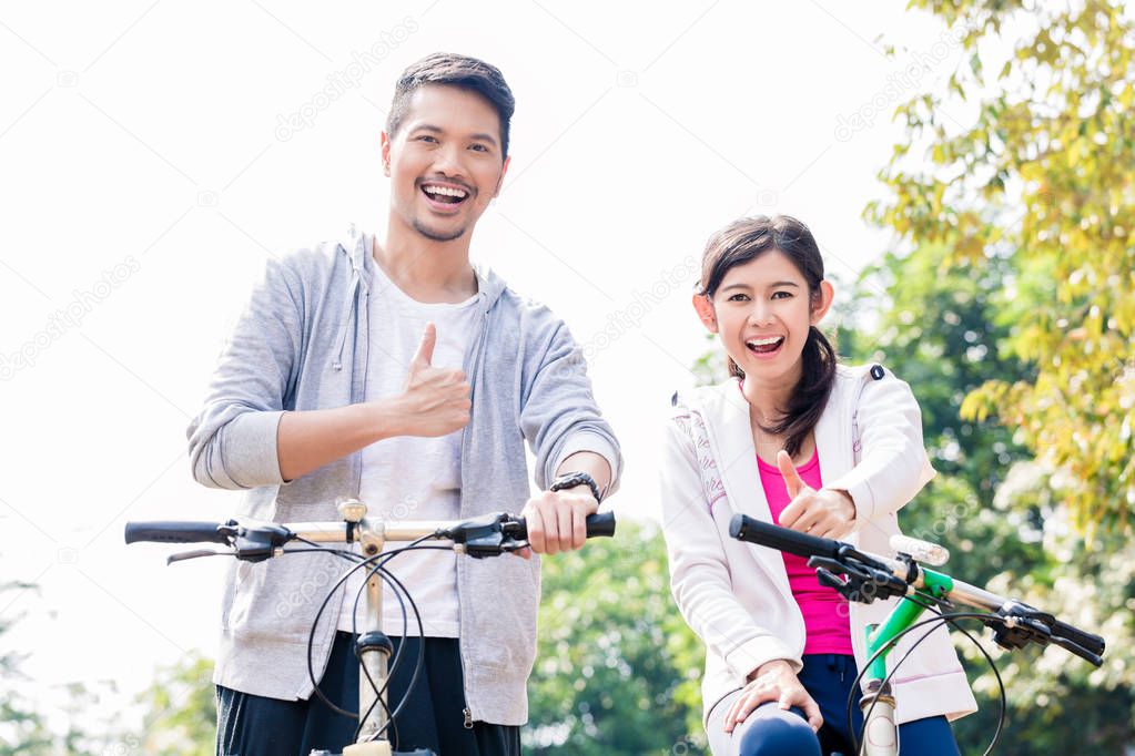 Young Asian couple laughing together while riding bicycles