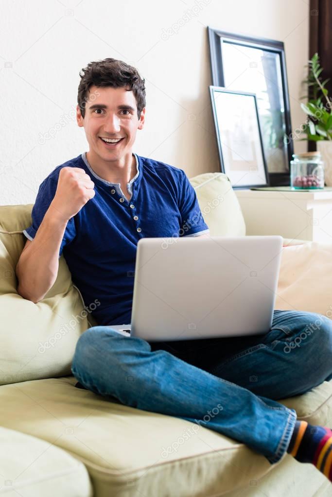 Young man looking at camera as a winner while using a laptop