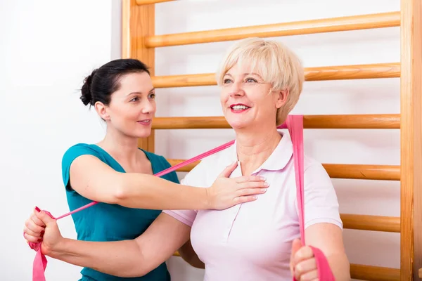 Physio auxiliando a mulher idosa durante o exercício com banda de poder a — Fotografia de Stock