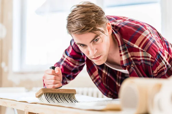 Hombre joven aplicando pasta a la superficie de una hoja de papel pintado dur —  Fotos de Stock