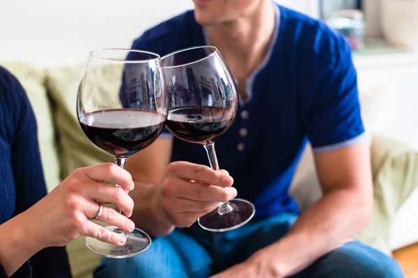 Romantisches junges Paar prostet sich mit Rotwein zu, während es auf dem Tisch sitzt — Stockfoto