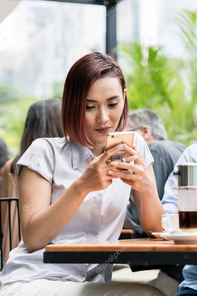 Portrait of a young Asian woman using a mobile phone at a coffee