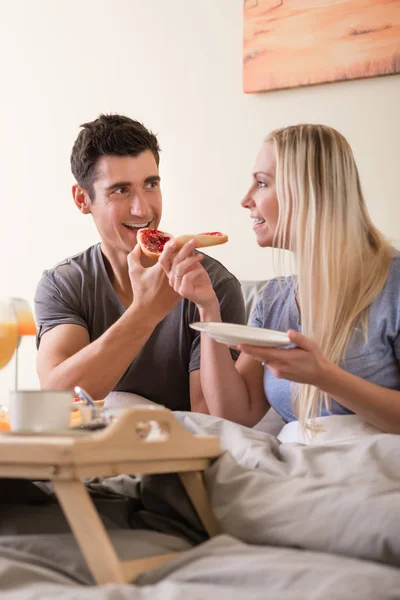 Mutlu genç çift yatakta kahvaltı yapıyor. — Stok fotoğraf