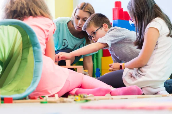 Ragazzo prescolastico che coopera con i bambini sotto la guida di Kindergar — Foto Stock