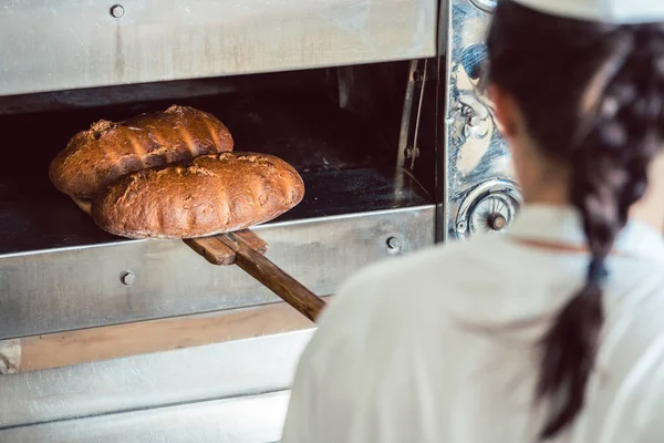 Baker getting fresh bread with shovel out of oven — Stock Photo, Image