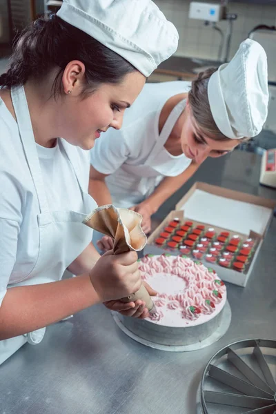 Confectioner women putting cream on cake — Stock Photo, Image