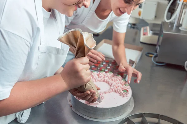 Confectioner women putting cream on cake — Stock Photo, Image