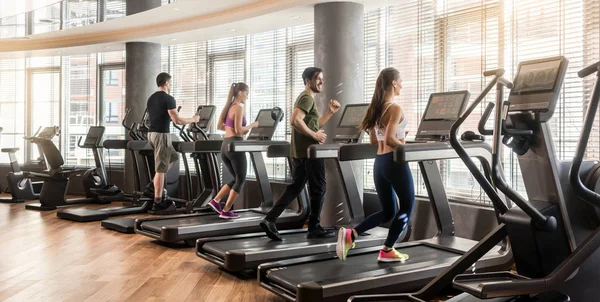 Groupe de quatre personnes qui courent sur des tapis roulants dans une salle de fitness — Photo