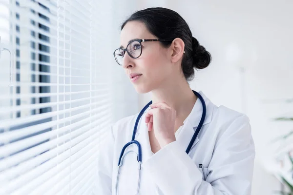 젊은 여성 의사는 창문을 통해 보고 있는 동안 공상 — 스톡 사진