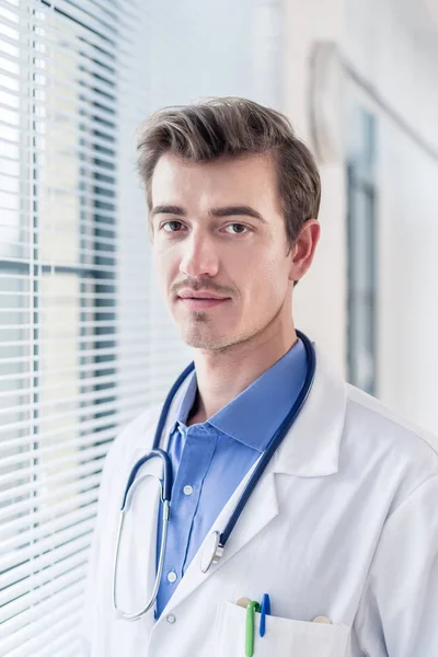 Портрет молодого серйозного лікаря, який дивиться на камеру з фірмою — стокове фото