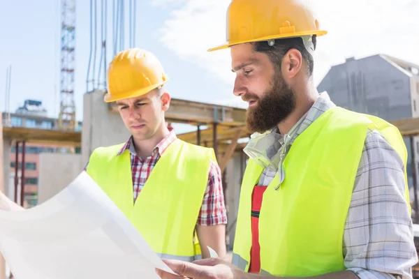 Dos jóvenes trabajadores de la construcción analizando juntos el plan de un —  Fotos de Stock