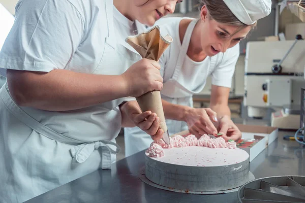 Confectioner women putting cream on cake — Stock Photo, Image