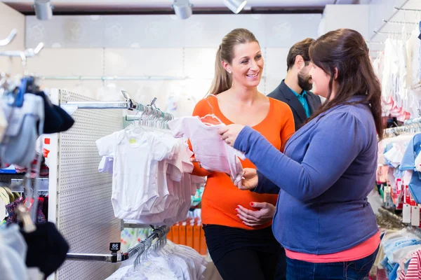 Salesperson with couple buying baby clothes in shop — Stock Photo, Image