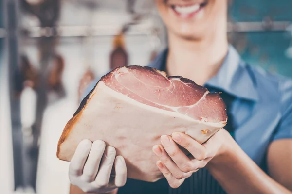 Giovane macellaia con prosciutto crudo in macelleria che vende carne — Foto Stock