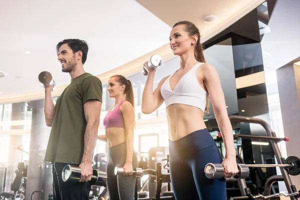 Tre unga människor ler medan alternerande hantel bicep curl — Stockfoto