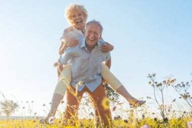 Happy senior man laughing while carrying his partner on his back clipart