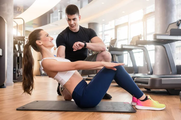 Личный тренер назначает время молодой подходящей женщине во время изометрических упражнений — стоковое фото