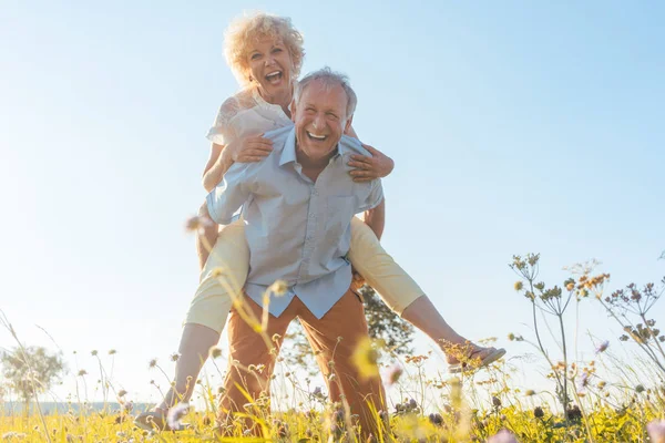 Glücklicher Senior lacht, während er seine Partnerin auf dem Rücken trägt — Stockfoto