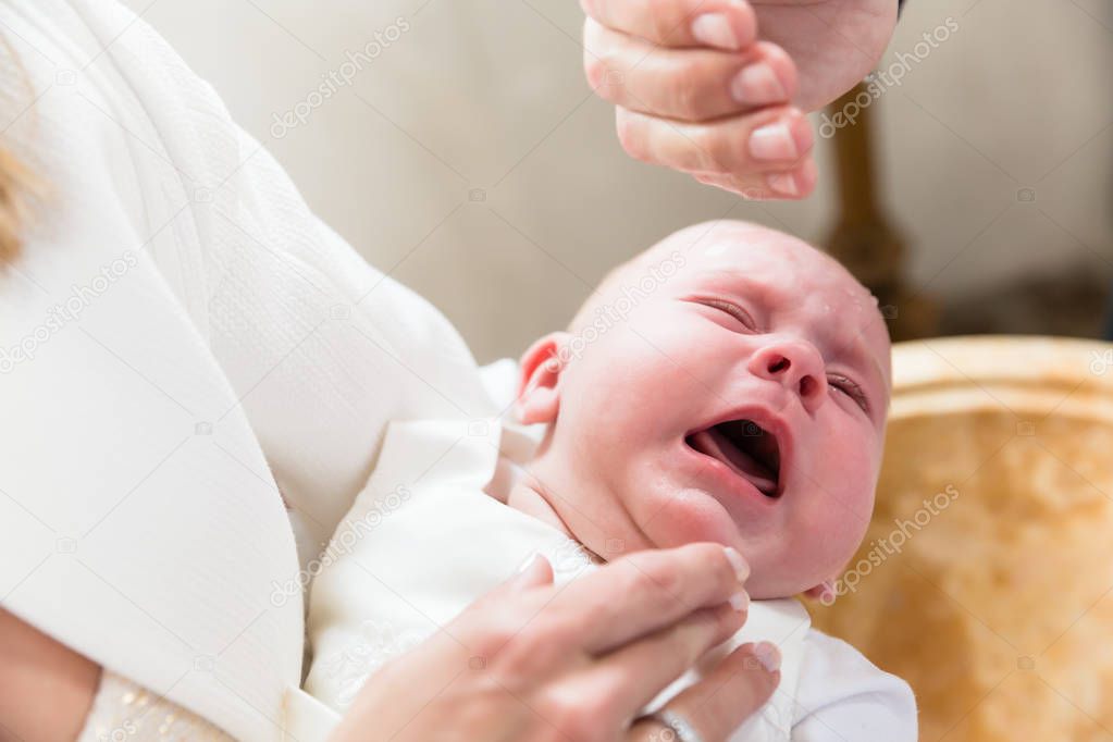 Baby is crying at christening while the priest pours holy water